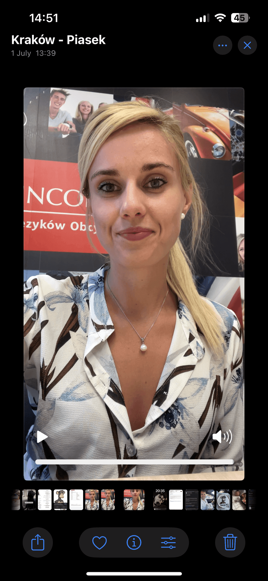 Woman taking a selfie indoors with a poster of smiling people and cars in the background.