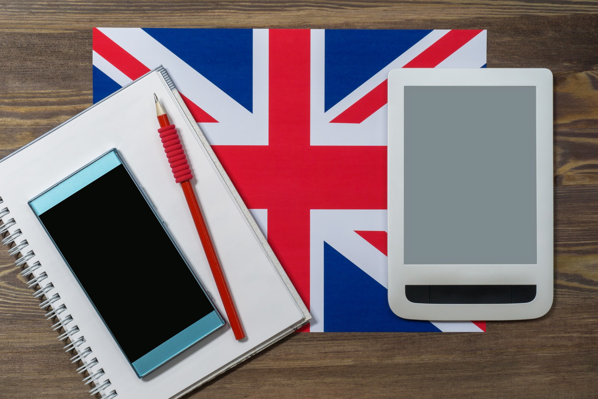 Phone, notebook, red pencil, tablet, the flag of the United Kingdom on a brown wooden background. English language course online . Layout for advertising, flat lay